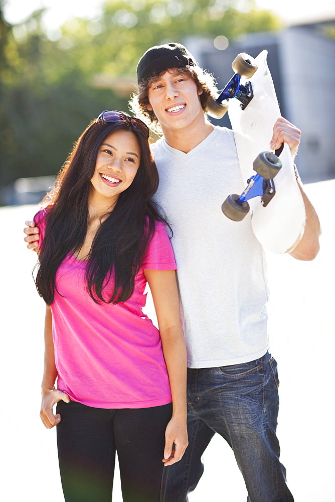 Young multi-racial couple posing with skateboard