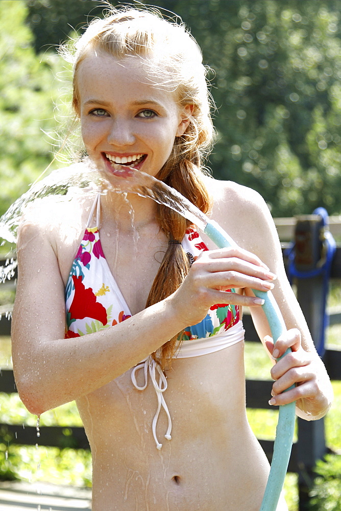 Teenage girl (14-15) wearing bikini drinking water from garden hose