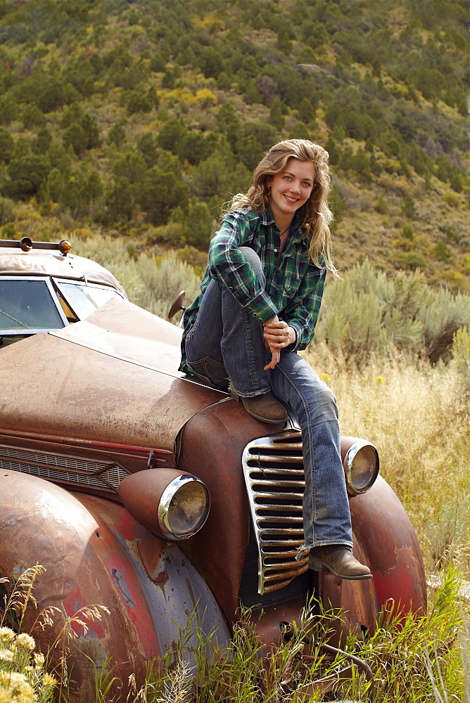 USA, Colorado, Portrait of woman resting on abandoned truck in desert