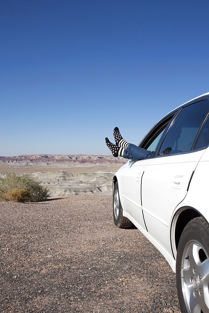 USA, Arizona, Winslow, Woman sticking feet out of car window parked in desert