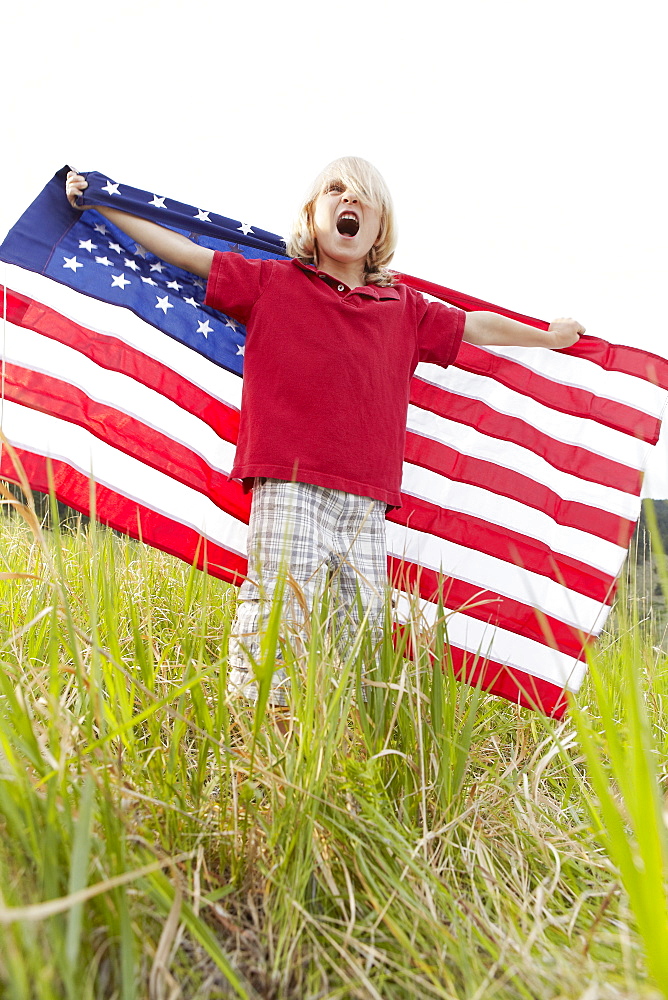 Boy (6-7) waving American flag in meadow