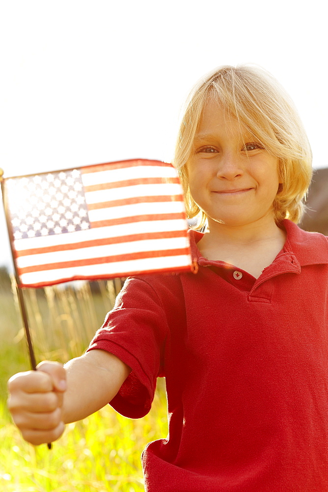 Portrait of boy (6-7) waving American flag in meadow