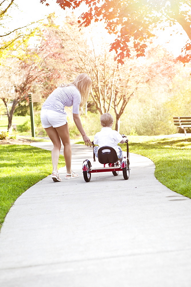 Mother and son (2-3) riding tricycle in park