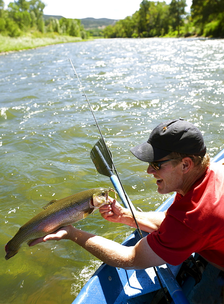 USA, Colorado, Man sitting in fishing boat, holding large trout