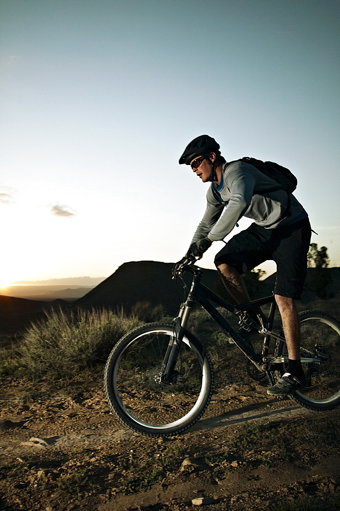 Man mountain biking at sunset