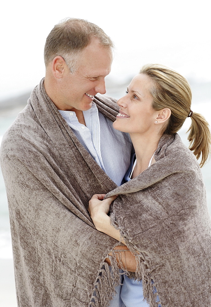 Portrait of couple wrapped in blanket on beach