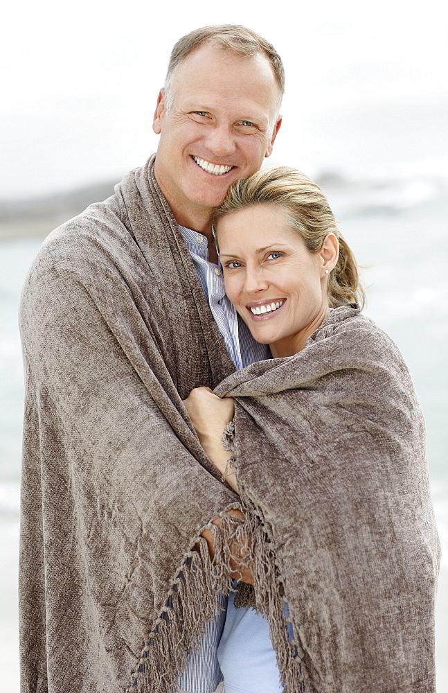Portrait of couple wrapped in blanket on beach
