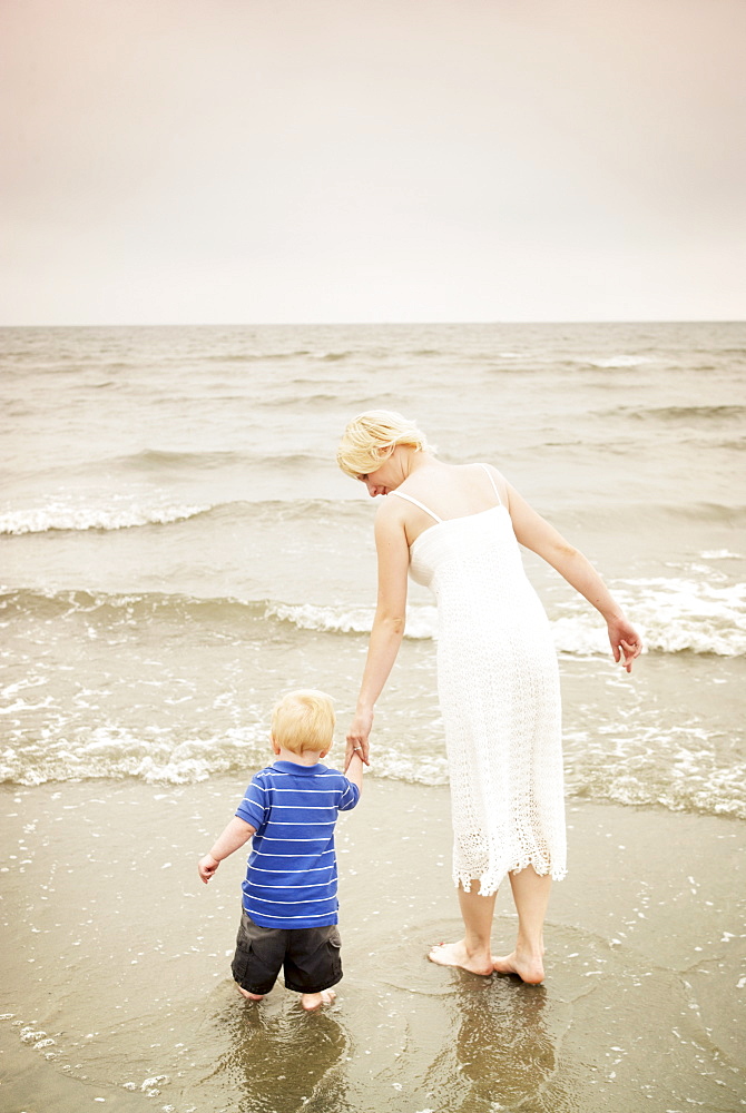 Mother and child walking hand in hand at the water's edge