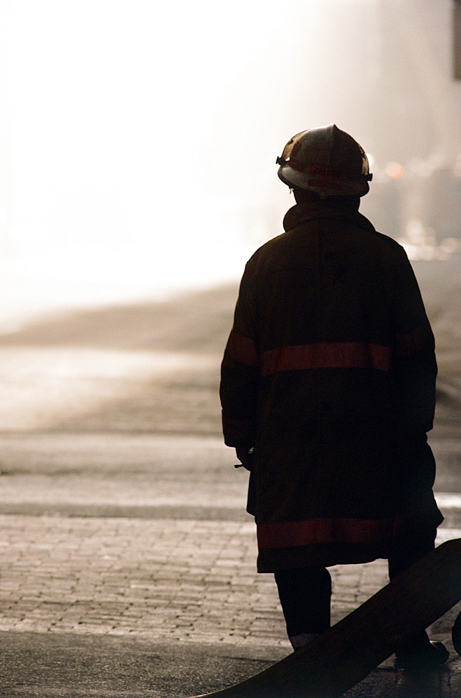 Silhouette of fireman looking at smoke in distance