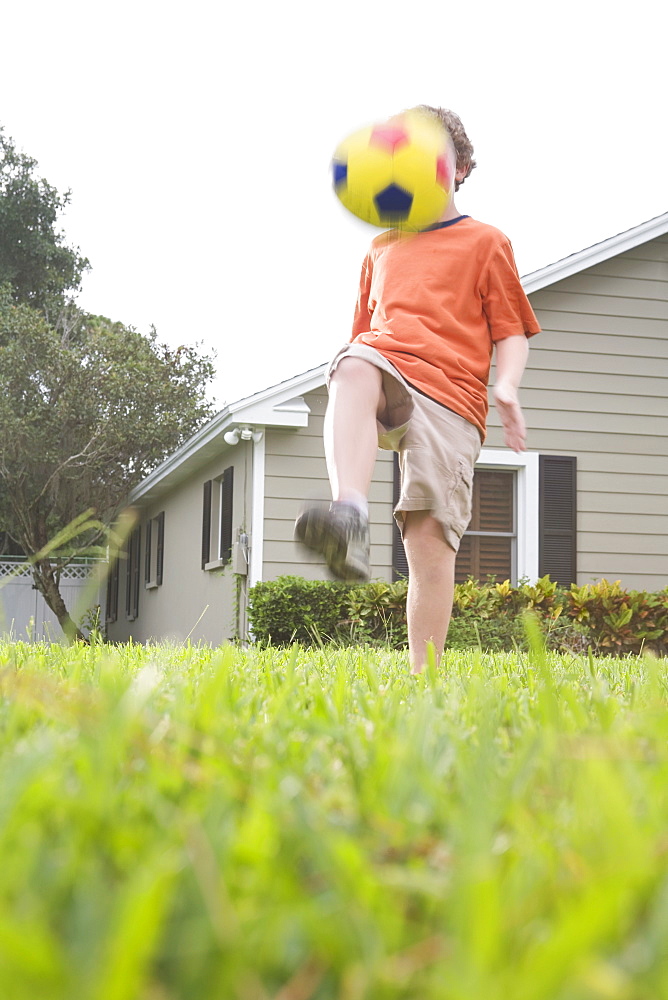 Boy in backyard kicking soccer ball