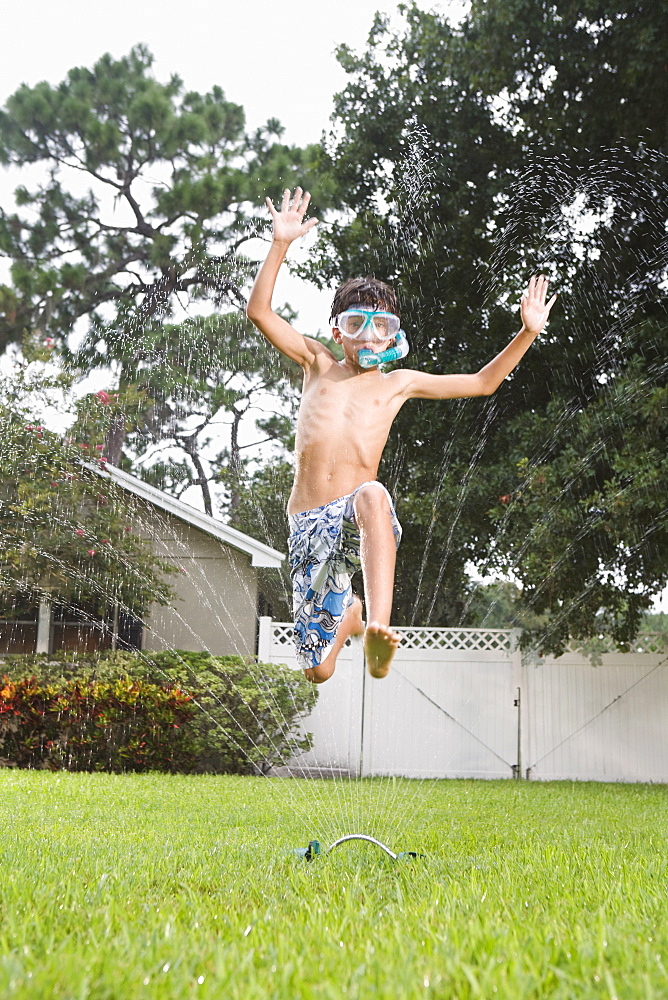 Boy with snorkeling mask running through sprinkler