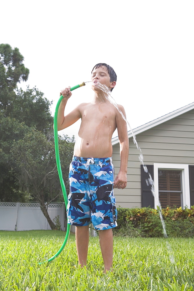 Boy drinking from garden hose in backyard