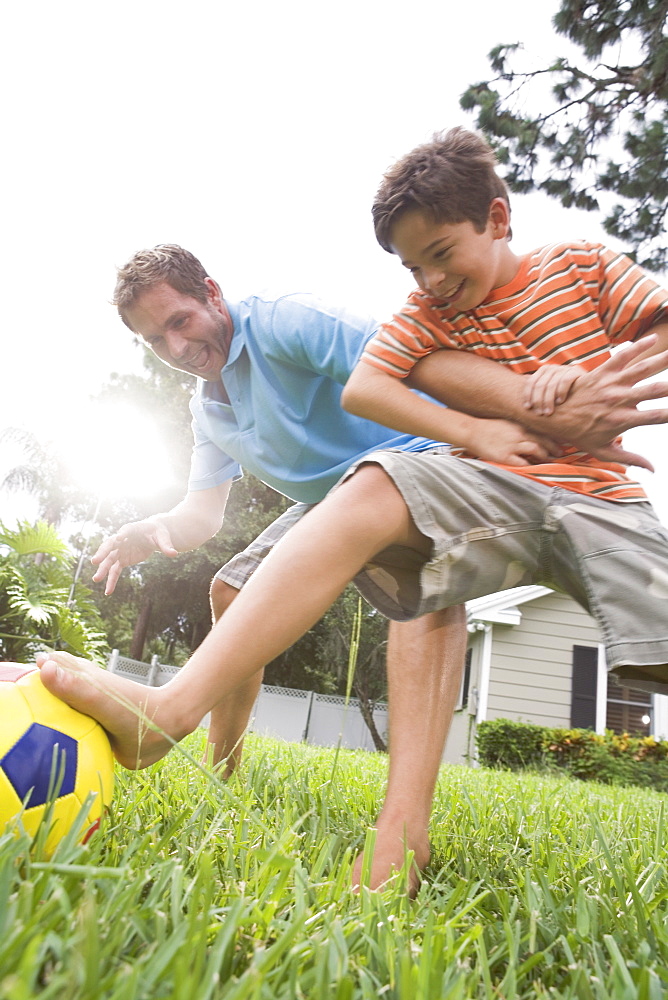 Father and son playing soccer in backyard