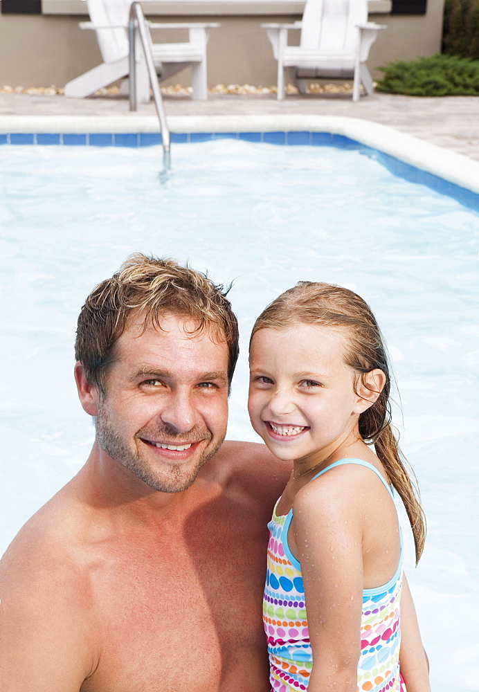 Father and daughter posing by swimming pool