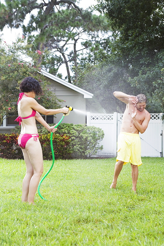 Woman spraying man with hose in backyard