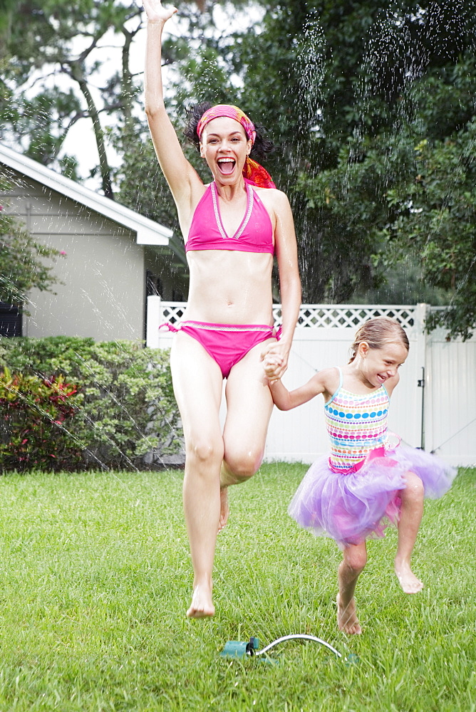 Mother and daughter running through sprinkler