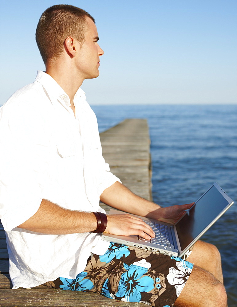 Young man using laptop on dock