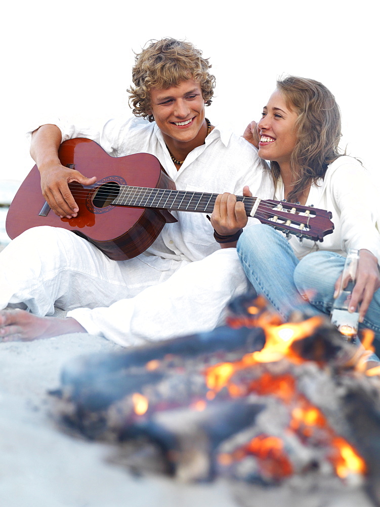 Young couple relaxing by campfire on beach