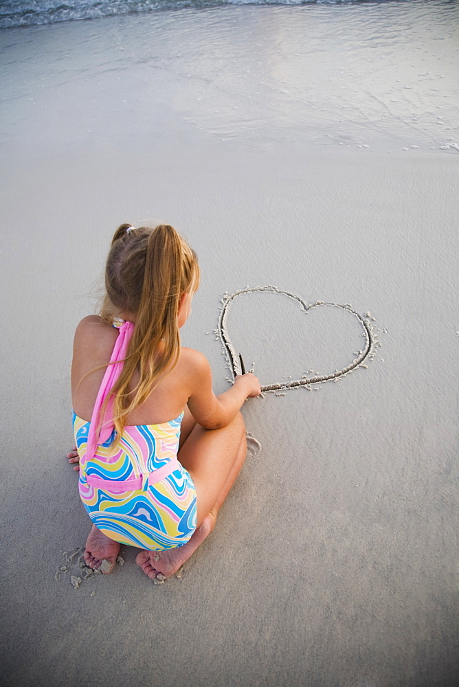 Girl drawing heart in sand, Florida, United States