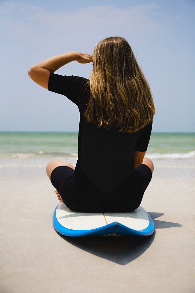 Girl sitting on surfboard, Florida, United States