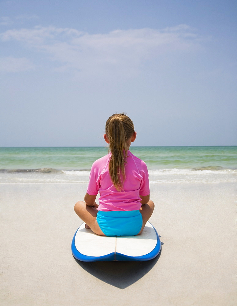 Young girl sitting on surfboard, Florida, United States