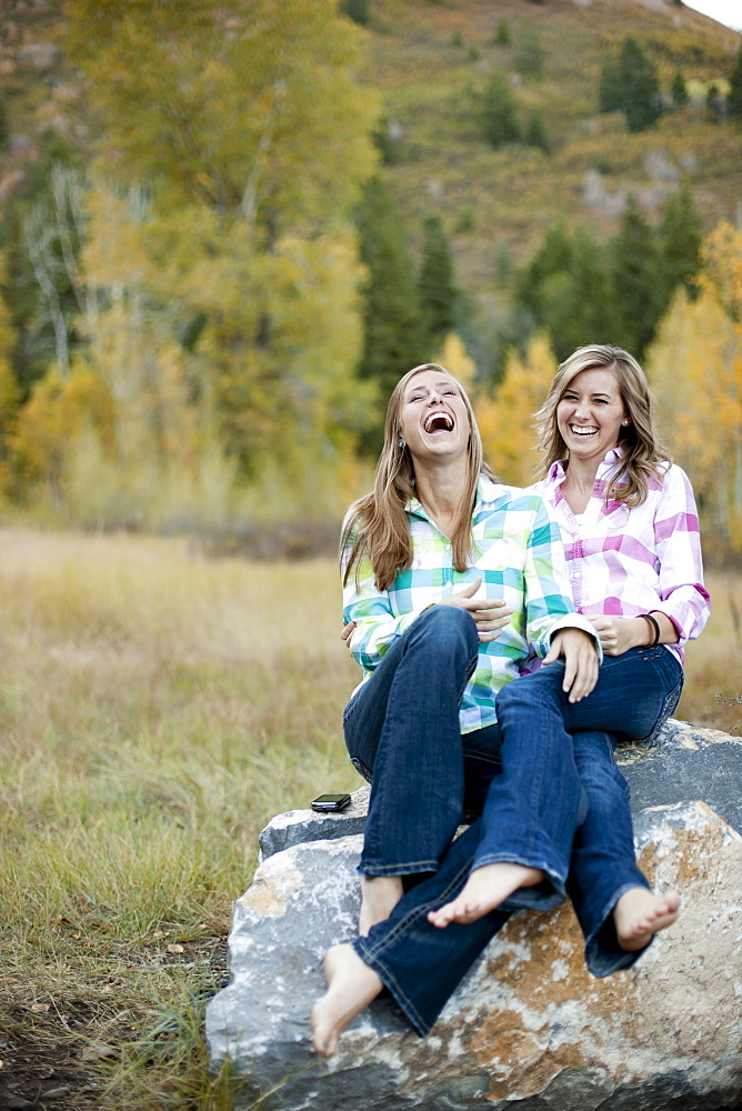 USA, Utah, Sundance, Two young women sitting on boulder and laughing