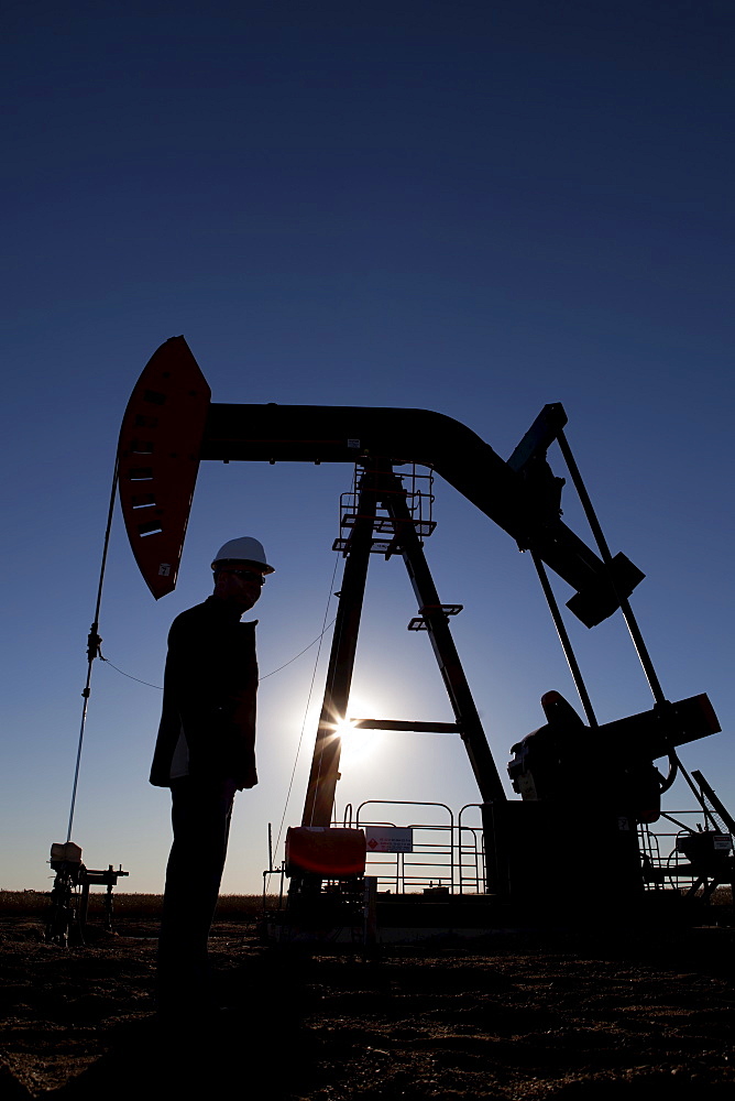 Silhouette of oil worker by pump jack on rig