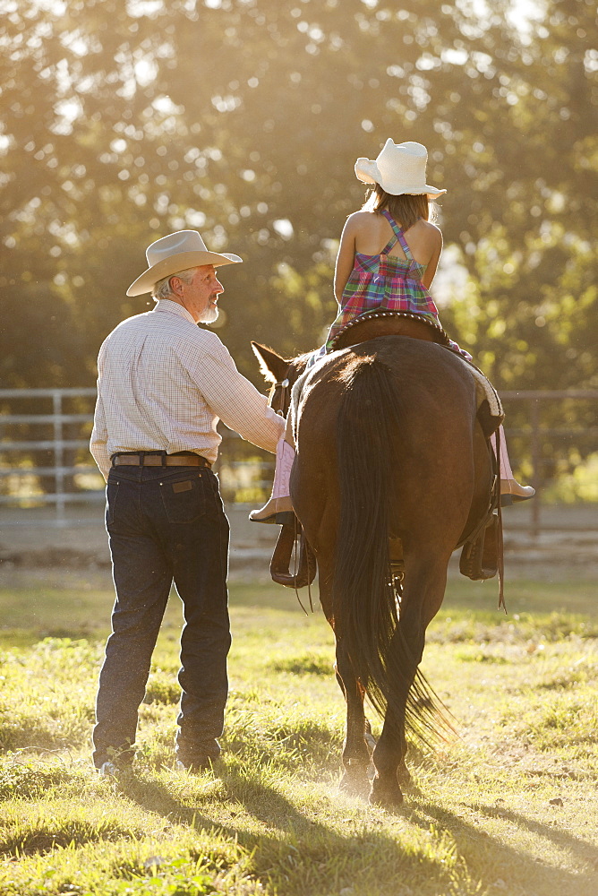 Senior man assisting granddaughter (8-9) horseback riding in ranch