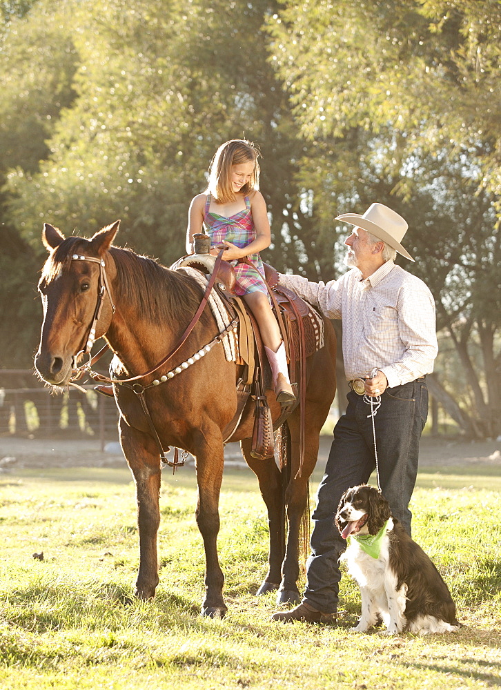 Senior man with dog assisting granddaughter (8-9) horseback riding in ranch