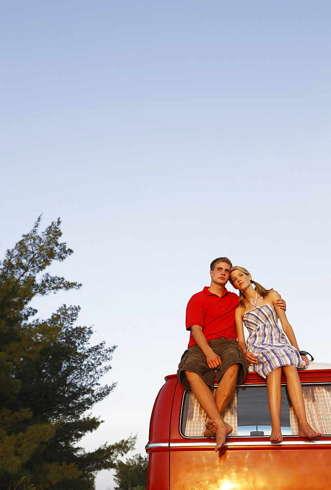 Couple watching ocean sunset from top of van
