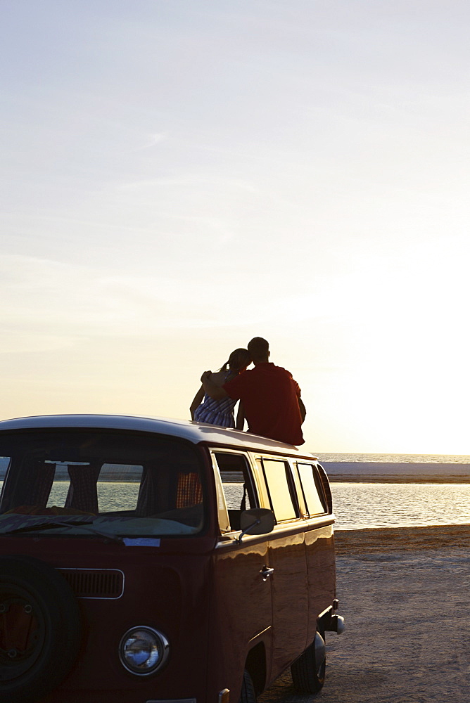 Couple watching ocean sunset from top of van