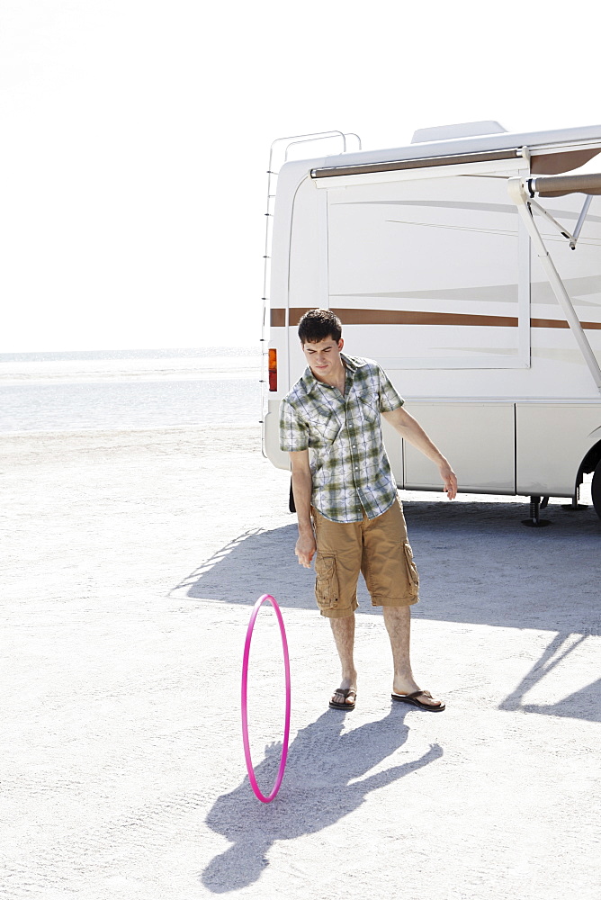 Young man spinning hula hoop on beach