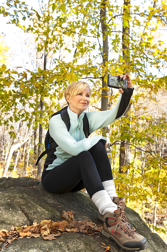 Female hiker photographing self on rock in forest