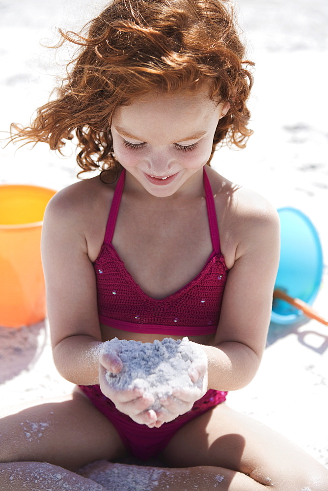 Girl in bikini cupping sand on beach