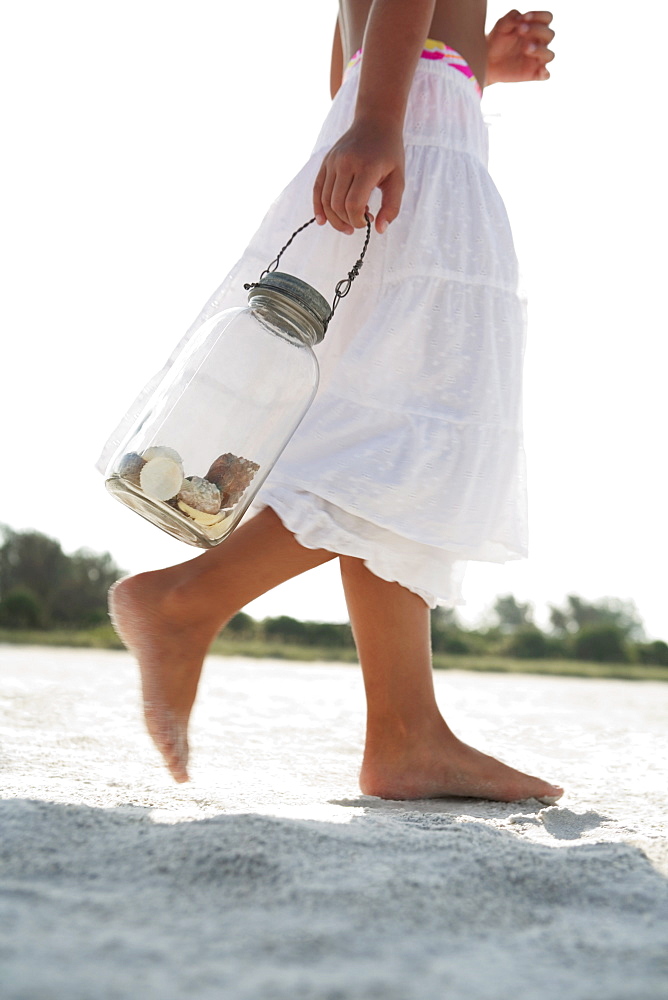 Girl on beach carrying jar of shells