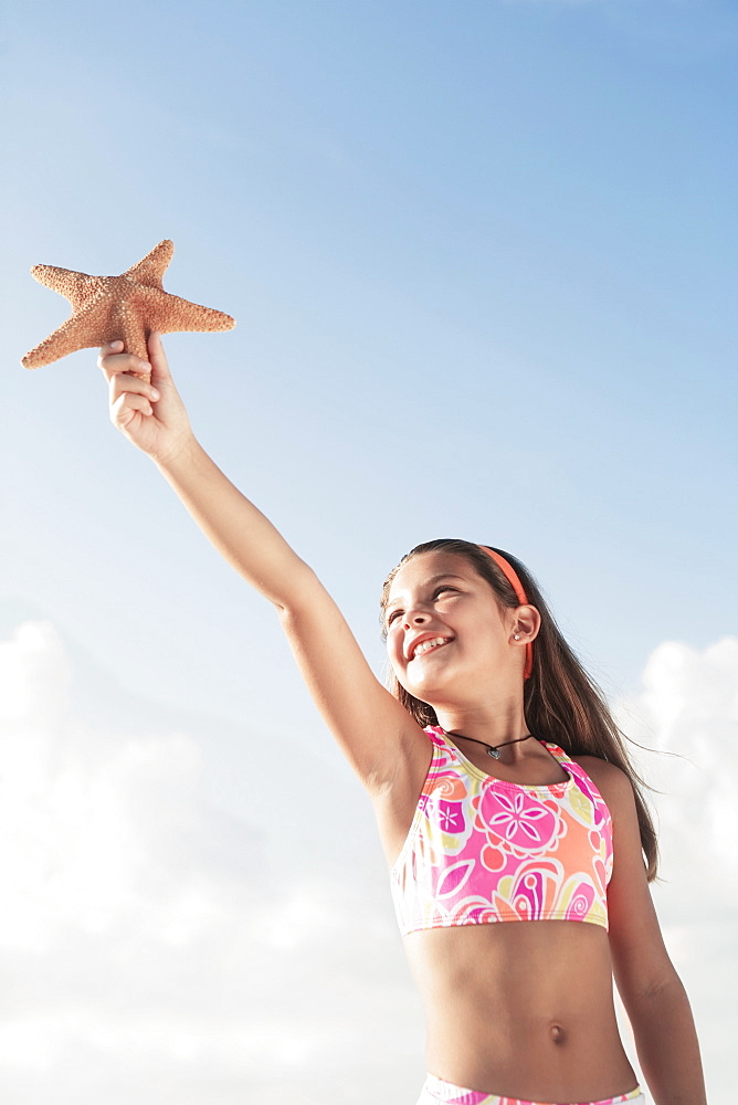 Girl in bathing suit holding up starfish