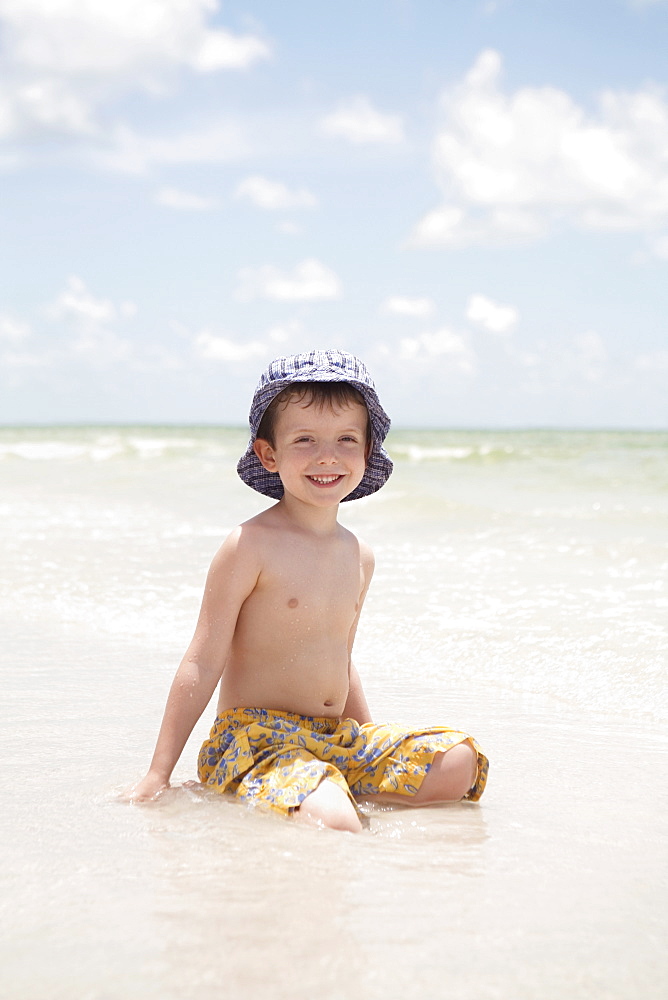 Boy sitting in shallow ocean