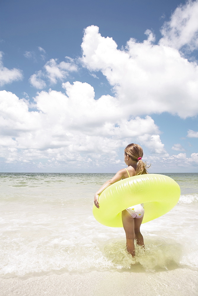 Girl carrying inflatable ring into ocean