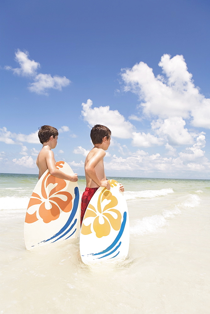 Boys holding skimboards in ocean