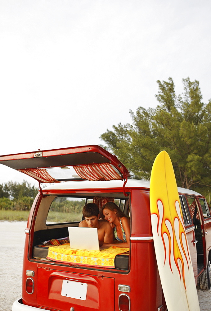 Young couple using laptop in van on beach