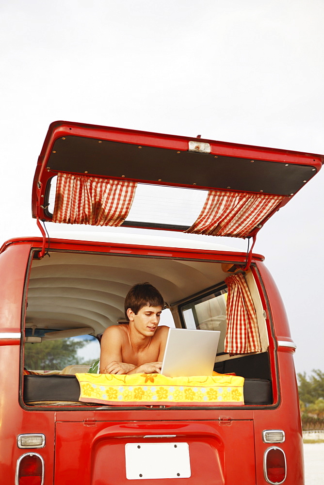 Young surfer using laptop in van on beach