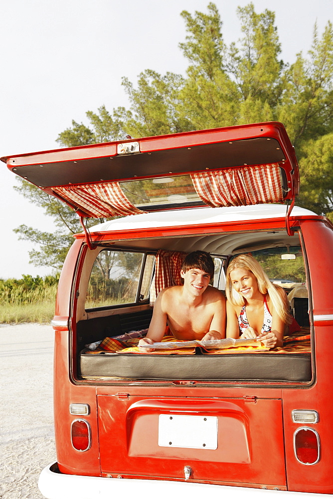 Teenage couple relaxing in van on beach