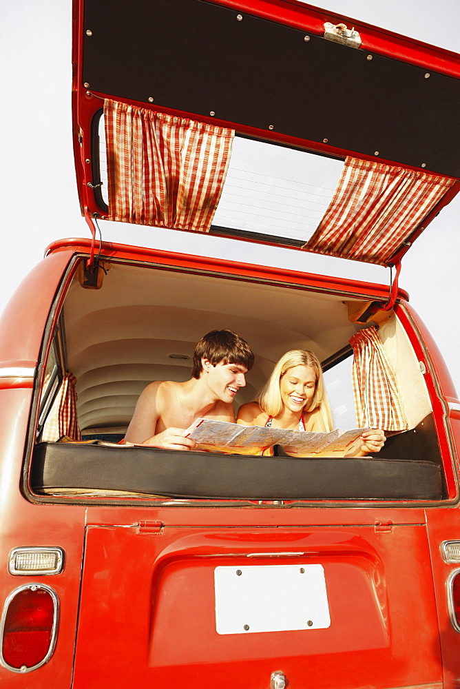 Teenage couple relaxing in van on beach