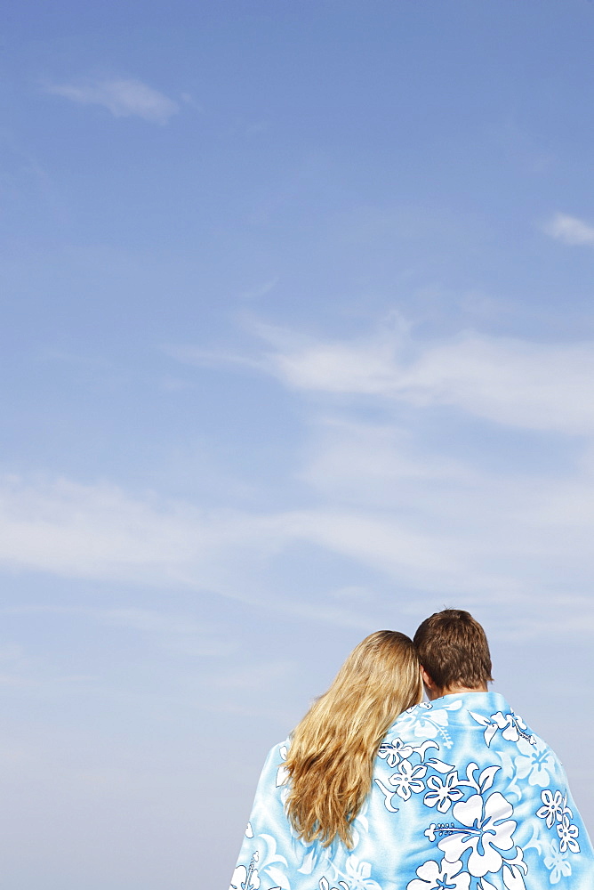 Teenage couple hugging under towel on beach