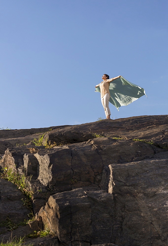 Mature woman standing on cliff with arms raised