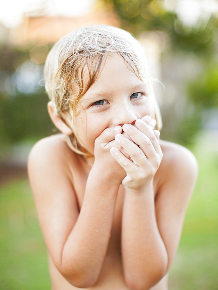 Portrait of boy (8-9) with hands covering mouth