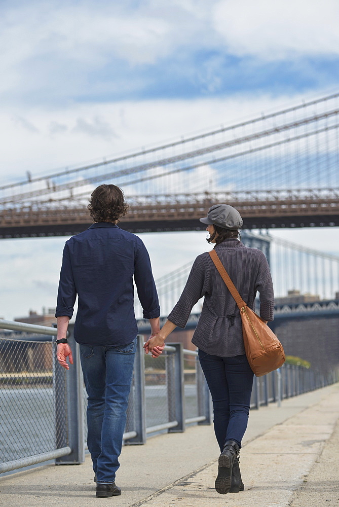 Rear view of couple walking on promenade, Brooklyn Bridge in background, Brooklyn, New York