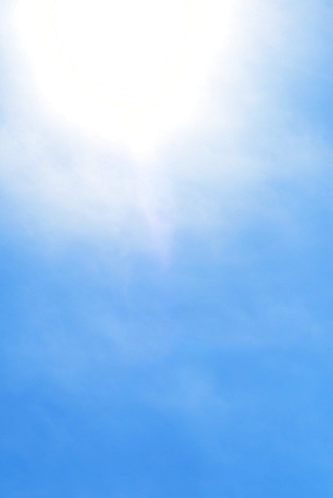 Sun behind small cloud on blue sky
