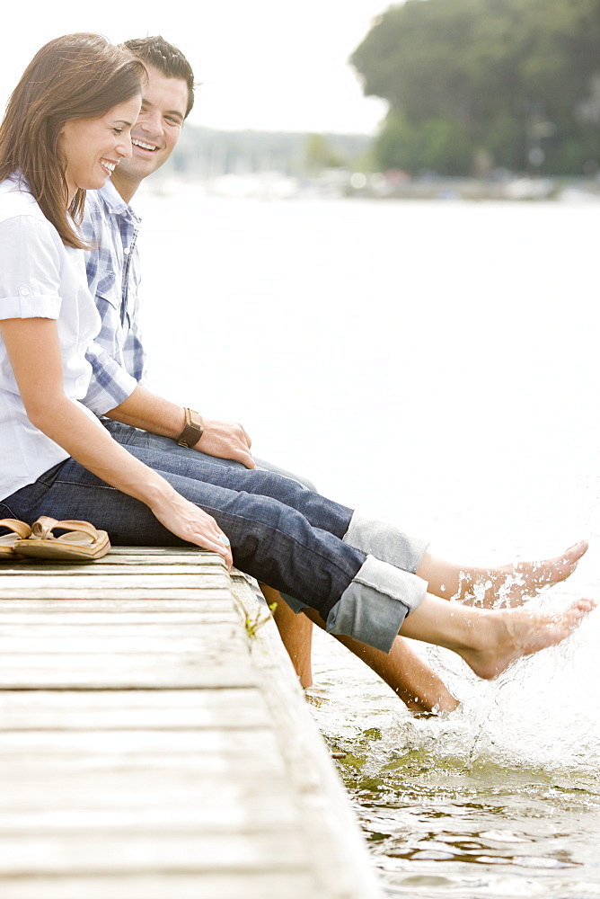 Couple sitting on dock and splashing feet in lake