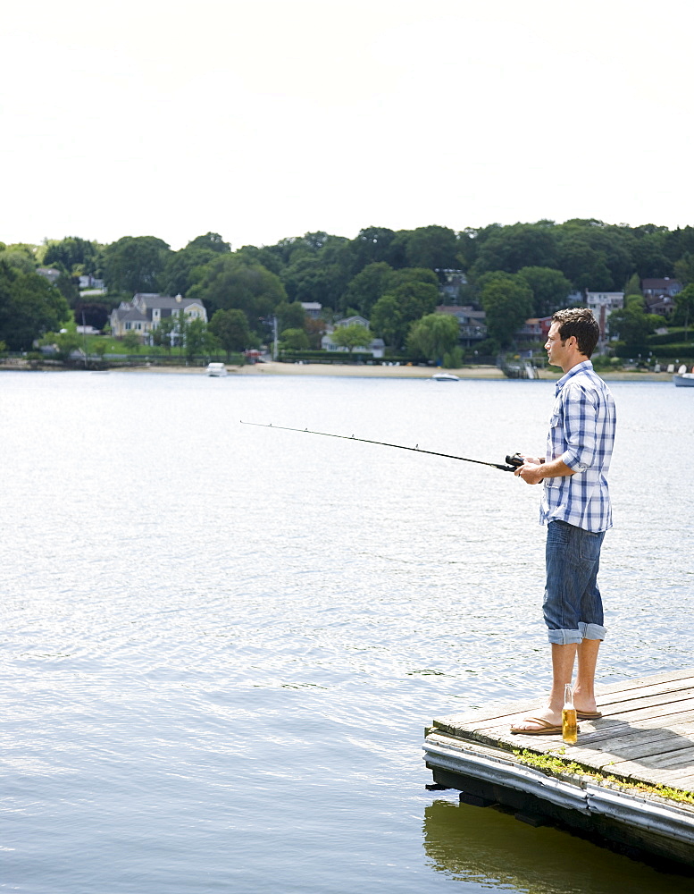 Man fishing off dock with beer at feet